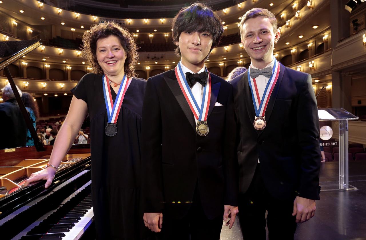 The three winners from the 2022 competition standing on stage and wearing their medals