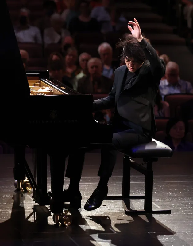 Yunchan Lim actively playing the piano with an arm raised up